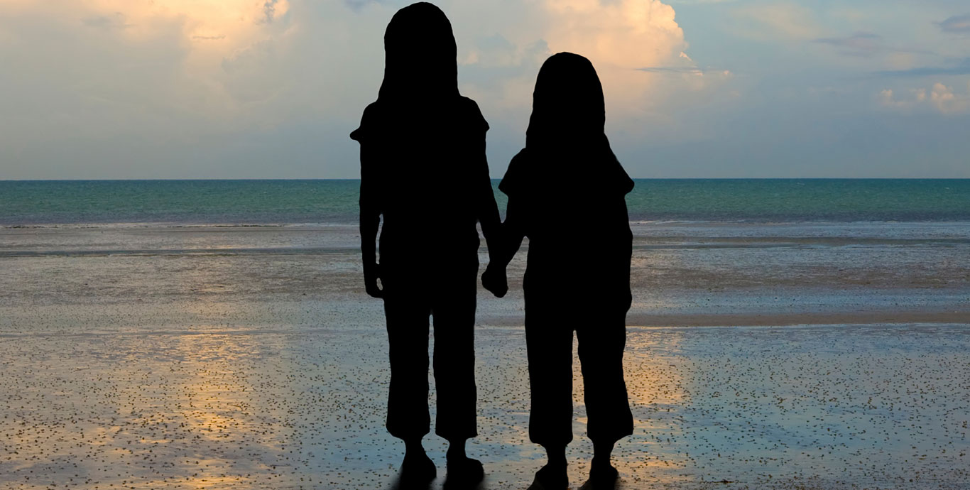 Sisters holding hands on the beach at sunset