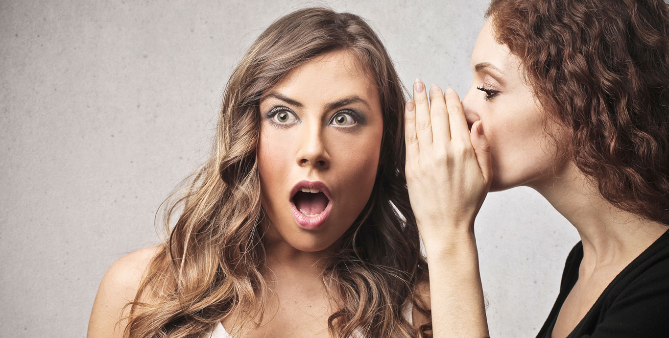 Woman whispering something to another woman who looks shocked