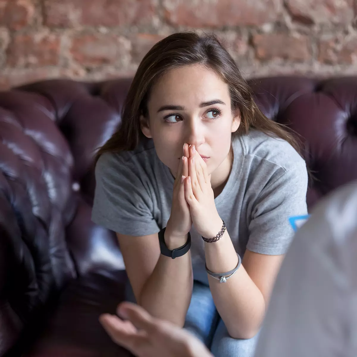 Young woman pressing her hands against her lips while sitting on the therapist's couch